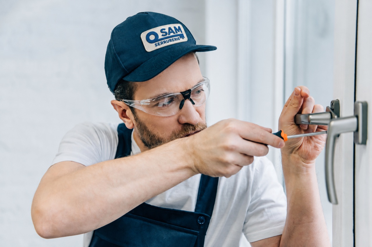 Photo d’illustration : un artisan ajuste la poignée d’une porte avec un tournevis